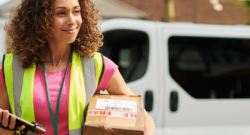 delivery woman carrier box and electronic device with wearing yellow safety vest with delivery van in the background